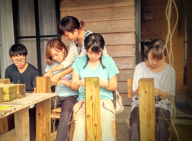 島で作られているアクセサリーの手伝いとして四つ編みを習って練習する学生ボランティア